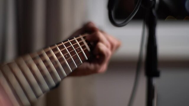 Close-up hands of unrecognizable guitarist singer man playing guitar and singing into microphone while recording song in home studio. Top view of condenser mic on recording session of acoustic guitar.
