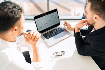 Two businessmen at laptop are watching chart of the company's income growth