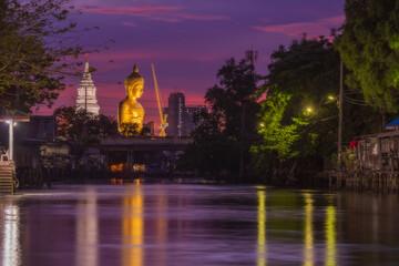 Fototapeta na wymiar Big golden buddha statue under construction at Wat Paknam Bhasicharoen temple at Twilight time, viewed from Klong Dan, Bangkok, thailand