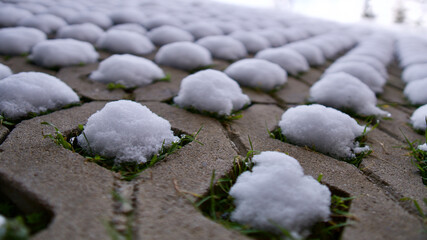 Fototapeta na wymiar Heaps of snow on the perforated garden stone. snow puddle.