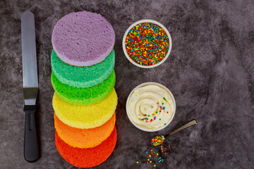 Assembling rainbow layer cake with white cream.
