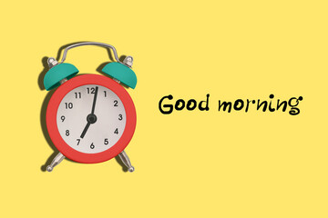 Colorful alarm clock on a yellow background with dough Good morning. The clock shows seven o'clock in the morning. Time to get up to work