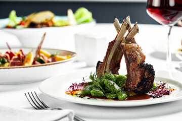 Grilled rack of lamb on a white plate with stewed bean pods. Grilled lamb with a glass of wine on a...