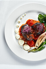 Braised beef cheeks with vegetables on a white plate Cooking beef cheeks in demigas sauce with grilled spinach leaves and carrots light background top view