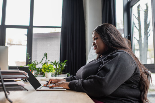 happy african american plus size woman typing on laptop keyboard in office.
