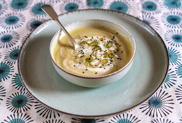 Flat lay photography of a vegan pumpkin cream soup and bread with selective focus. Vegetables recipe. Top view of an autumn puree of seasonal products with a retro pattern fabric tablecloth.