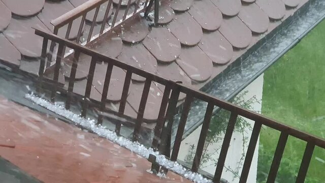 Close-up of a brown roof with snow guards and a gutter during a strong thunderstorm with hail falling down in summertime. Seen in Germany in June.