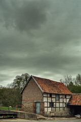 Historic half-timbered farmhouse in the countryside under a stormy dark sky.