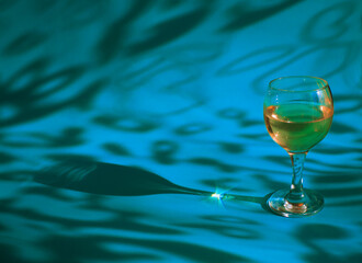 A glass of white wine or champagne on a blue background with sunshine shadow effect. The play of light and shadows creates a whimsical picture on the background