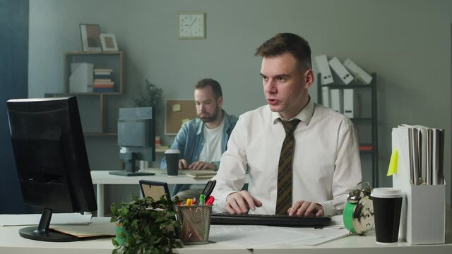 Irritated man in business uniform works in office, keypad stops working, angry employee breaking keyboard on the table, destroying everything in workplace. Bad mood, failure at work. 