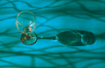 An empty wine glass on a blue background with sunshine shadow effect. The play of light and shadows creates a whimsical picture on the background. 