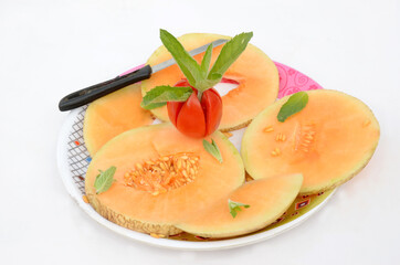 closeup sliced ripe orange muskmelon with red tomato mint and knife isolated on white background.