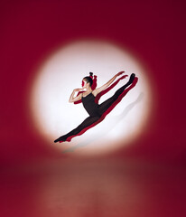 Fototapeta na wymiar Ballet dancer dancing over red studio background. Modern design. Contemporary colorful conceptual light as rising sun at Japan.