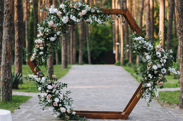 A beautiful wooden wedding arch in the form of a hexagon, decorated with natural flowers, stands on...