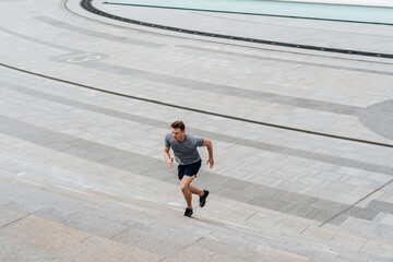 Fototapeta na wymiar Young athlete man runner running up and down on city stairs in summer on morning run, background urban city street. Sports training. Fitness cardio workout in fresh air, walk outside.