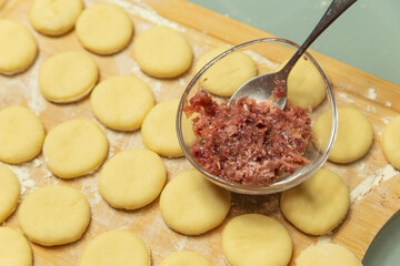 cut circles out of dough on a board with a bowl of stuffing