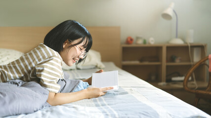 Young adult asian woman lay and relax reading book on bed.