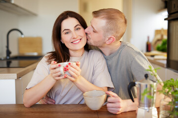 home, love and relationship concept - young couple kissing in modern kitchen