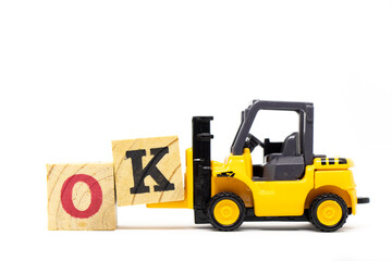 Toy forklift hold letter block k to complete word ok on wood background
