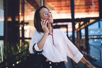 Fototapeta premium Cheerful adult woman talking on smartphone on terrace