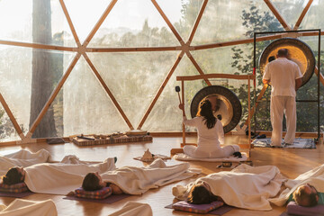 People in white robes hitting gong in bright room