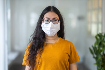 Portrait of asian female wears hygiene protective mask in orange dress doing while looking at camera in the consultation,Prevention of the spread of COVID-19 virus