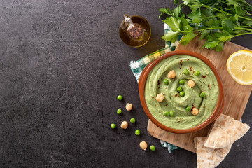 Green pea hummus on black background. Top view. Copy space