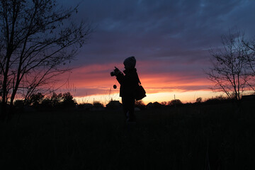Silhouettes of a boy with a camera on the background of sunset