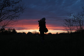 Silhouettes of a boy with a camera on the background of sunset
