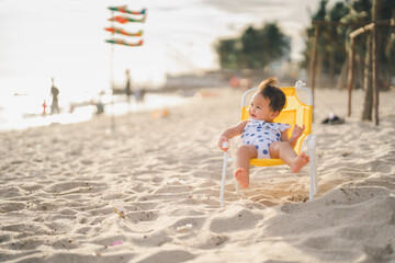 baby in white dress sit on the chair beach yellow color with smile happy and relaxing and the wind...