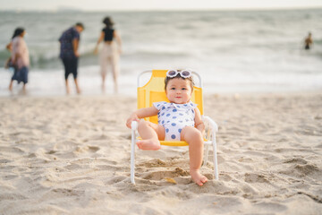 baby in white dress and sunglasses sit on the chair beach yellow color with smile happy and...