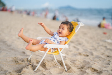 baby in white dress and sunglasses sit on the chair beach yellow color with smile happy and...