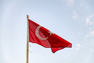 Turkish flag against blue sky with cumulus clouds.