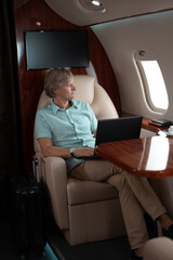 Attractive and successful businessman working on a laptop while sitting in the chair of his private jet