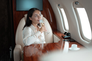 Successful young business woman traveler drinks champagne with her parthner during flight in private jet. Private jet planes advantages privacy, efficiency, luxury, security, flexibility. 