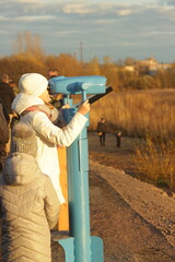 A girl looks through panoramic binoculars on a viewing platform in autumn park.