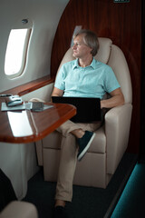 Attractive and successful businessman working on a laptop while sitting in the chair of his private jet