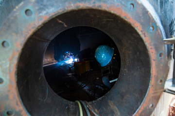 Male worker wearing protective clothing and repair welding sparks industrial construction tank oil inside confined spaces.
