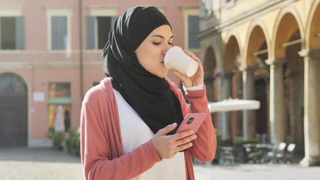 young muslim woman wearing hijab headscarf using smart phone walking in the city center,arab girl holding smartphone mobile texting messaging,online shopping communication,social network concept