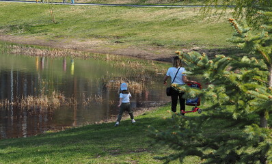 Spring warm day off. Mom walks in the park near the pond on a green lawn with a child.