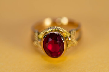 Real gold ring with red  gemstone close up macro shot on yellow surface.