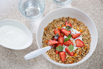 Bowl of granola with fresh strawberries and yogurt, elevated view on a beige marble background, horizontal shot