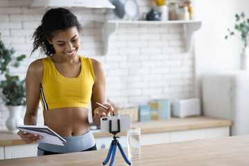 Handsome  African American woman fitness vlogger record streaming video about fitness and a healthy lifestyle at home in the kitchen, young female blogger shoot social media vlog on smartphone