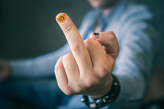 businessman unhappy. The middle finger is shown by a man in a blue shirt. FCK is written on a yellow nail, the design of a men's manicure. An obscene gesture to the camera. Negative emotion.