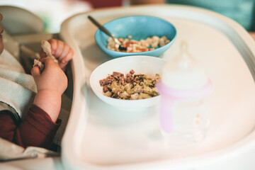 bébé qui regarde son repas et croise les mains, assit sur une chaise haute