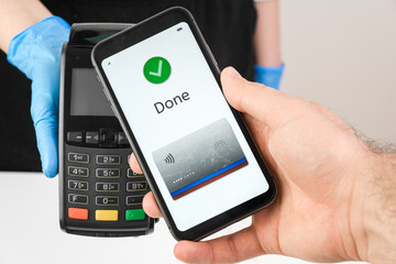 Close up of woman hand in rubber gloves holding a pos terminal or swiping machine and man hand holding a smartphone with app for payment. 