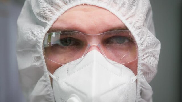 Close-up of overworked doctor or researcher dressed in protective suit ppe mask in laboratory in hospital, male nurse wearing medical uniform, portrait of tired man chemist in protect safety glasses. 