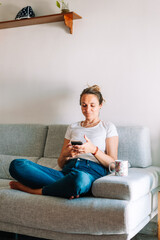 Obraz premium Portrait of confident young woman talking on cellphone at home. Girl sitting on coach and calling up her boyfriend. Wireless communication concept 