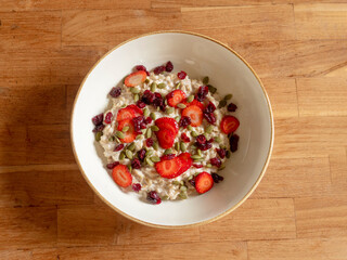 A bowl of oatmeal with strawberries on a wooden table. View from above.