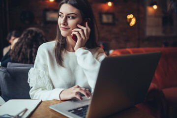 Smiling woman speaking on phone and browsing laptop